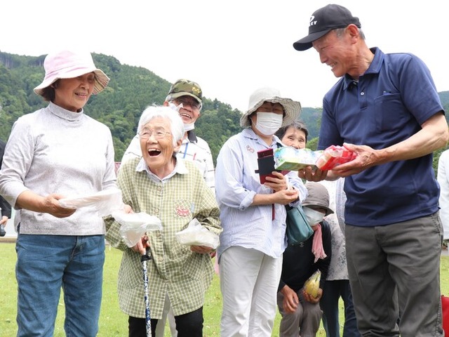 ドローンで配送された刺身やヨーグルト等の食料品を受取り笑顔の住民 (田野口地域振興センター)